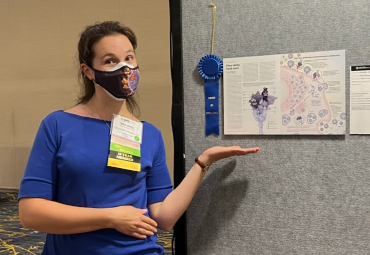 A picture of Veronica Falconieri Hays (white woman with brown hair, blue shirt, and wearing a mask) standing next to a poster image with a blue ribbon next to it.
